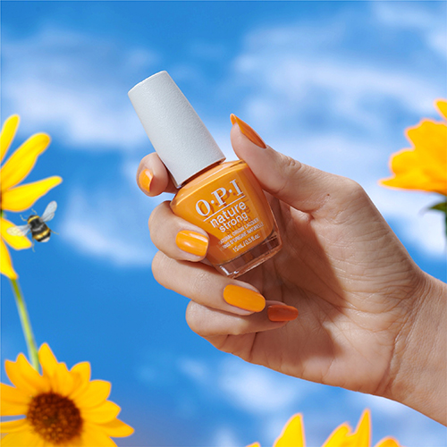 Hand holding orange OPI Bee the Change Color nail polish bottle with blue-sky and sunflowers