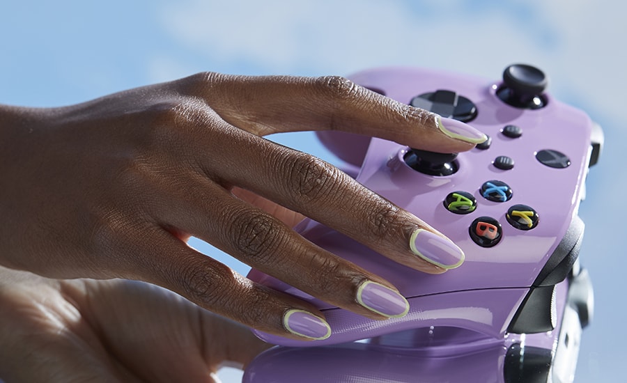 A hand with painted nails in the Achievement Unlocked shade from OPI Play the Palette collection with the Xbox Wireless Controller