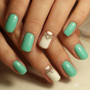 Light green nail polish with some accessories on a white nail