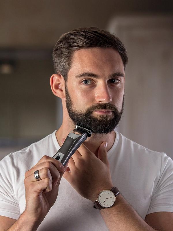 A handsome young man shaving his beard while sporting a ring, a watch, and a white T-shirt