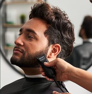 A barber uses a Wahl trimmer to shave a man's beard.