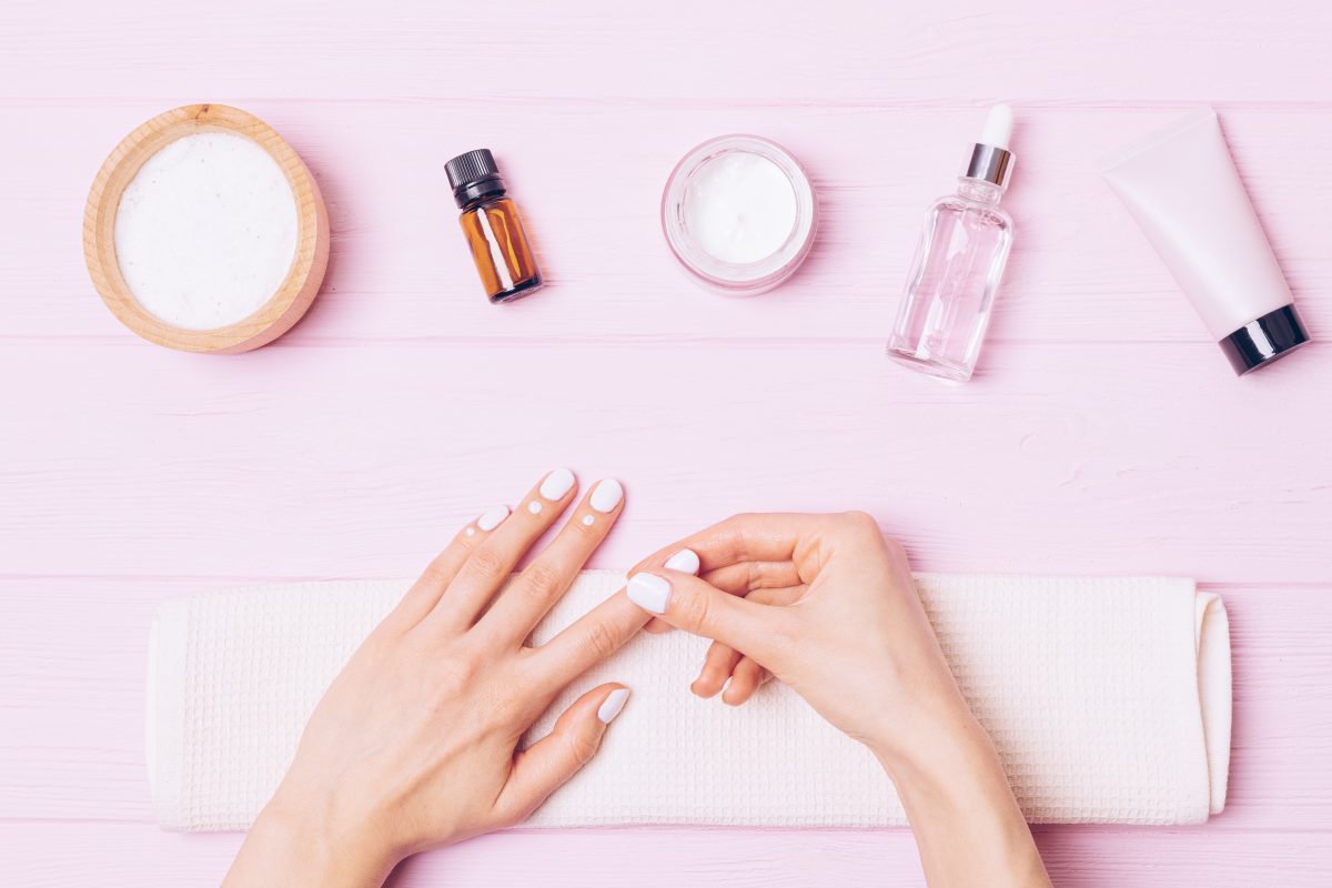 Nail care, female hands apply nourishing cuticle cream on pink background, top view. Healthy Nails
