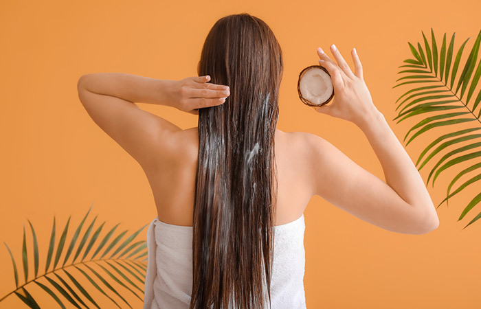 Beautiful young woman applying coconut oil mask on her hair against color background

