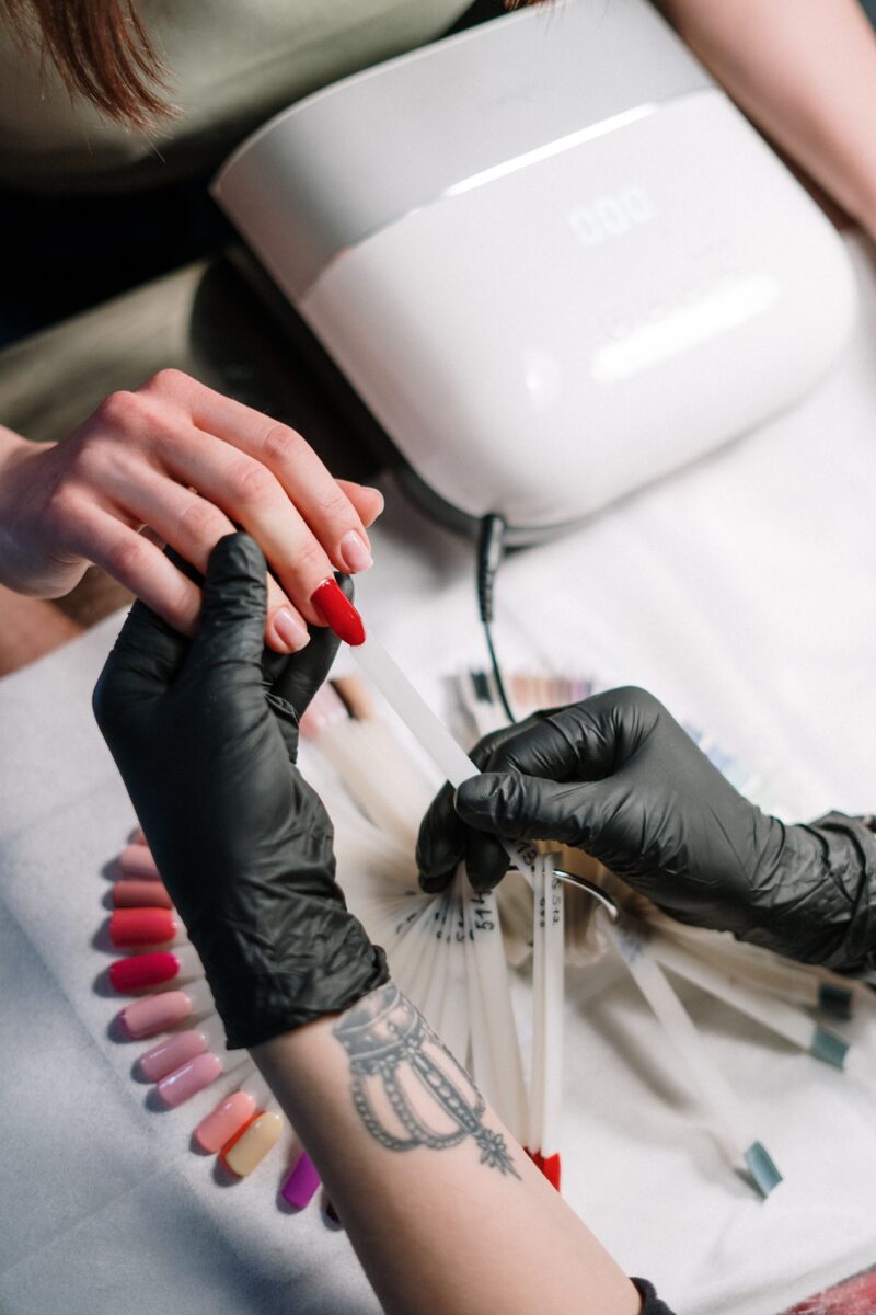 A nail technician's hand is holding a customer's hand in a beauty salon while choosing the best nail shape and color for the client's nails. Set of different nail tip shapes on a multicolor nail polish palette for client choice.