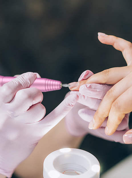 A nail technician uses an electric nail file drill with a carbide bit model 2-1-2 in a beauty salon.