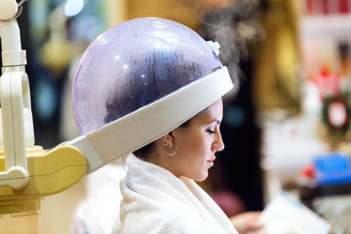 Portrait of beautiful young woman drying hair under machine in a beauty salon.