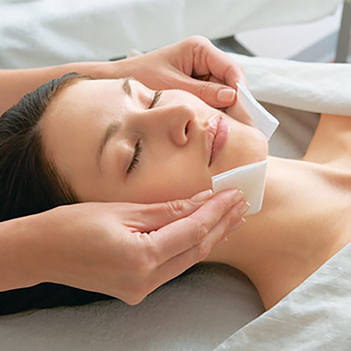 A therapist is using one of the most important tools of spa disinfectants, cleansing wipes, to clean the client's face.