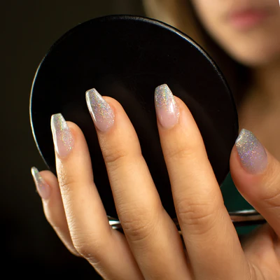 A faceless woman holds a mirror and wears fabulous glittery nail art designs on her nails.