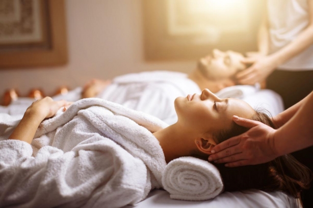 Two clients are on the clean massage bed wearing bathrobes, and the therapist is doing massages to their heads. Salon and spa disinfectants