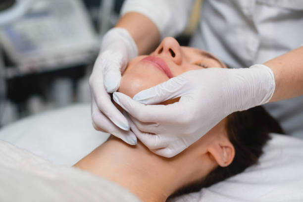 A therapist in a spa center wearing white gloves while doing massage for the client's face