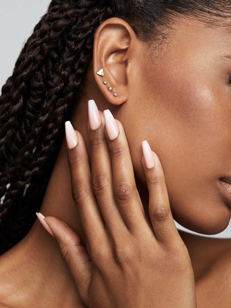 A faceless woman with curly hair and fabulous nails wearing four earrings
