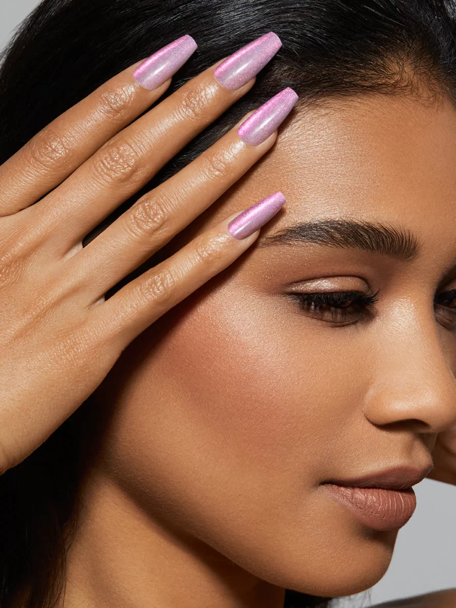 A woman with purple nails is posing with her hands on her face.