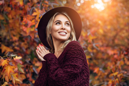 A beautiful woman wearing a hat and sweater in autumn leaves.