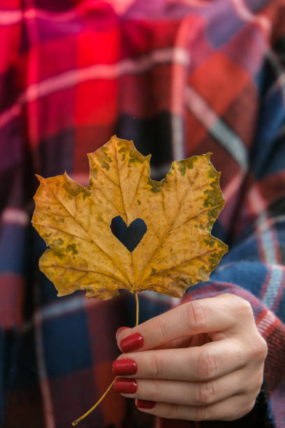 A woman holding a leaf with a heart on it, her nails are painted with a red nail polish shade