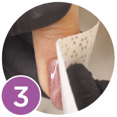 The third step for applying the Gelish Pure Velvet Magnet Gels. A faceless nail technician is holding a nail with a pink gel manicure on it while cleansing it.