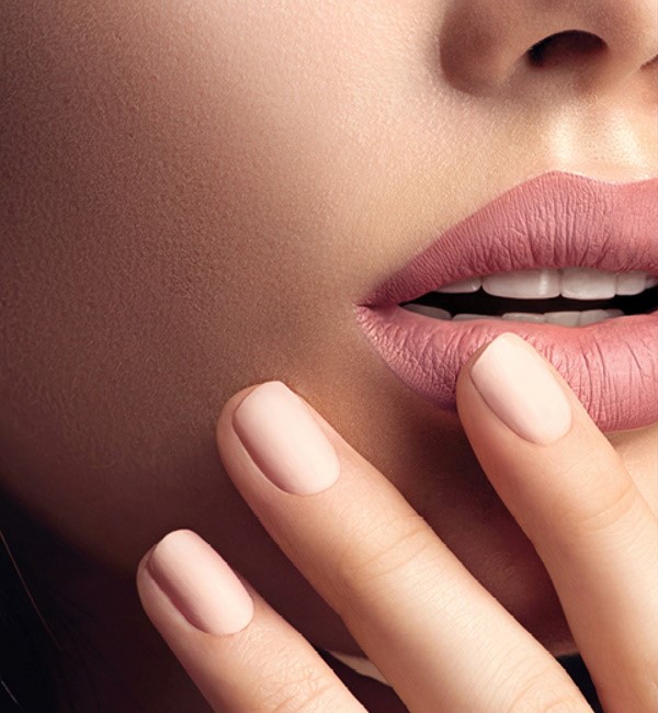 A close-up of a woman perfectly matching her pink lipstick with her nails painted in a light pink shade