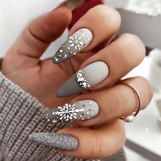  woman's nails adorned with grey and white polish featuring snowflake designs.