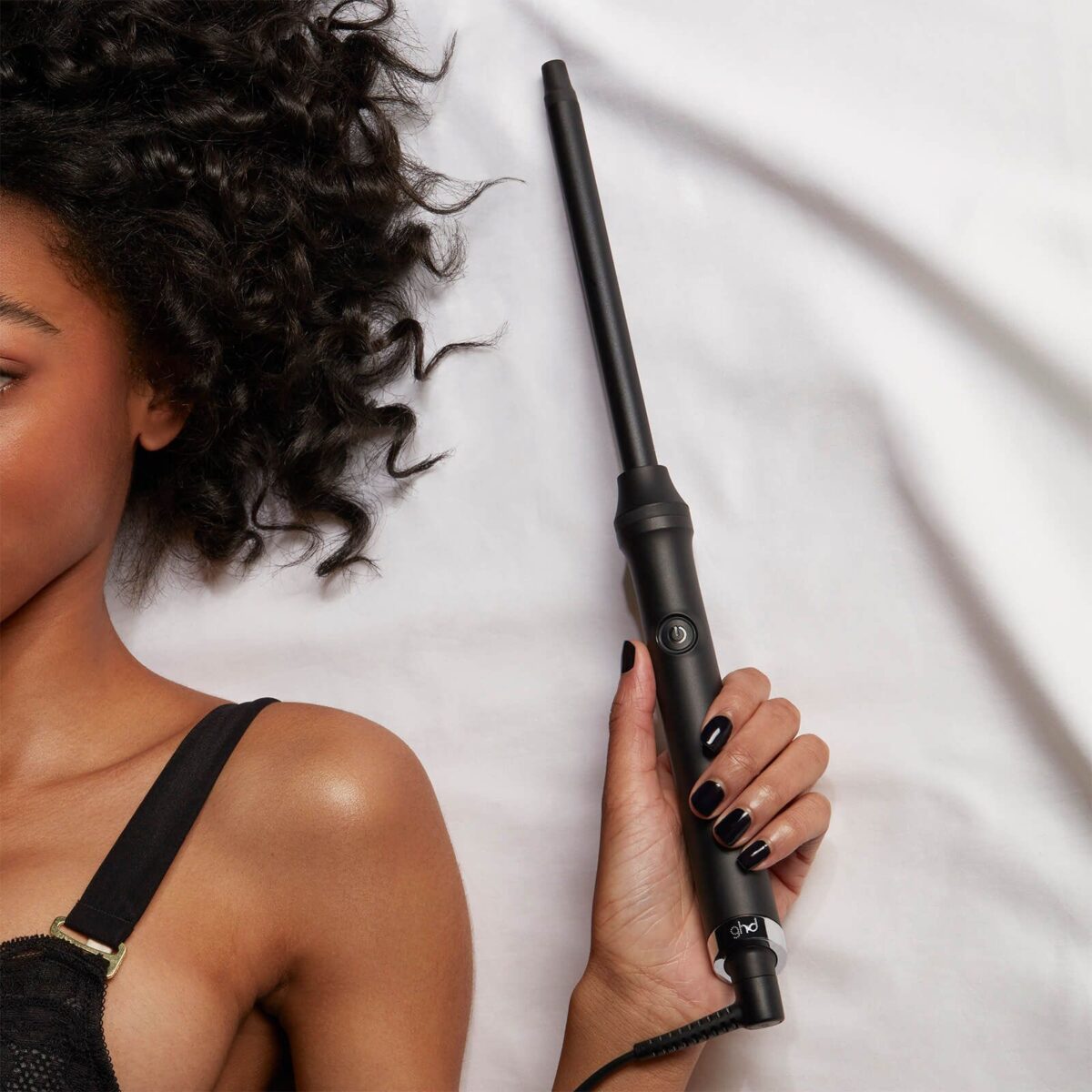A black woman laying on a bed holding a curling iron.