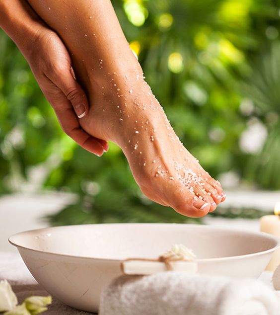 A woman's foot receiving a scrub in a bowl of sea salt.