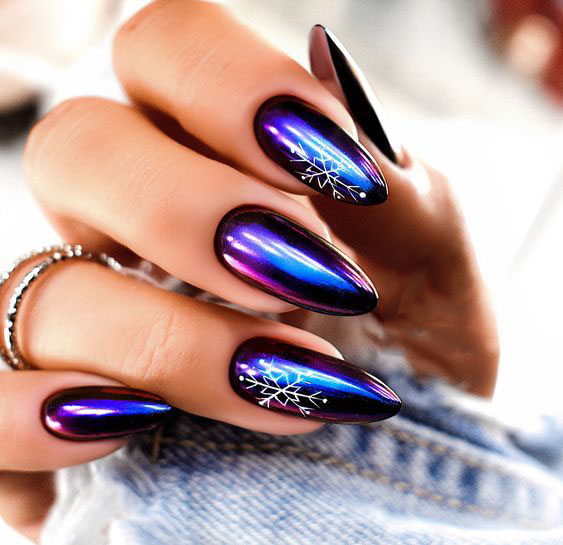 A woman's hand with purple and bold blue nails adorned with snowflake designs in white. Winter nail art trends