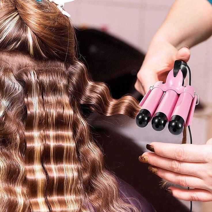 A woman is getting her brown hair done with a triple barrel curling iron by a hair professional