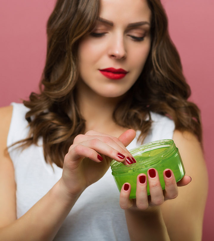 A stunning woman, her long wavy brown hair flowing gracefully, donned in a white shirt, holding a hair gel bottle, while her nails boast a vibrant Red nail shade that perfectly complements her matching red lipstick.
