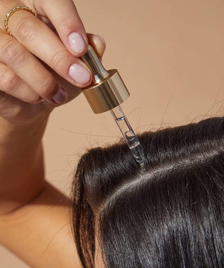 A faceless woman is applying a hair serum to her black hair