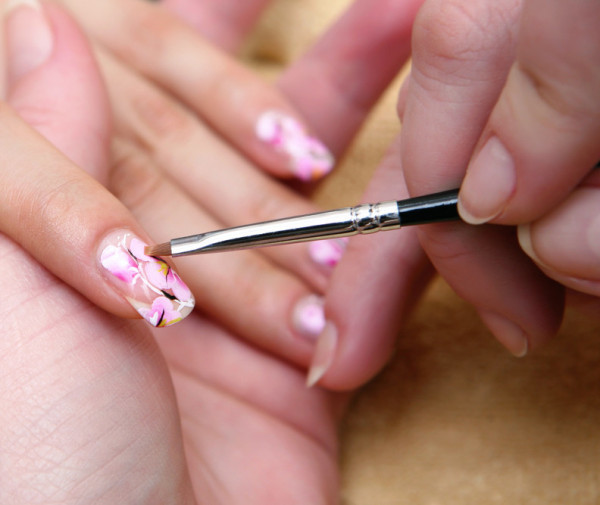 A faceless nail technician is applying a manicure with floral nail designs to the client's nails.
