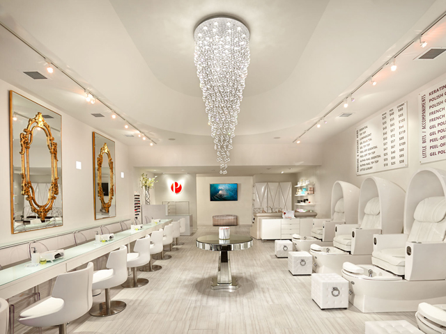 A nail salon with white manicure and pedicure chairs and a chandelier i the muddle.