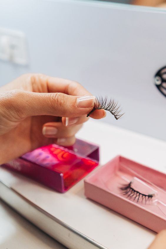 A woman is applying Ardell lashes in front of a mirror.