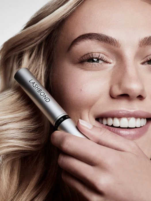 A blonde, beautiful woman holds the new Olaplex LashBond Building Serum.