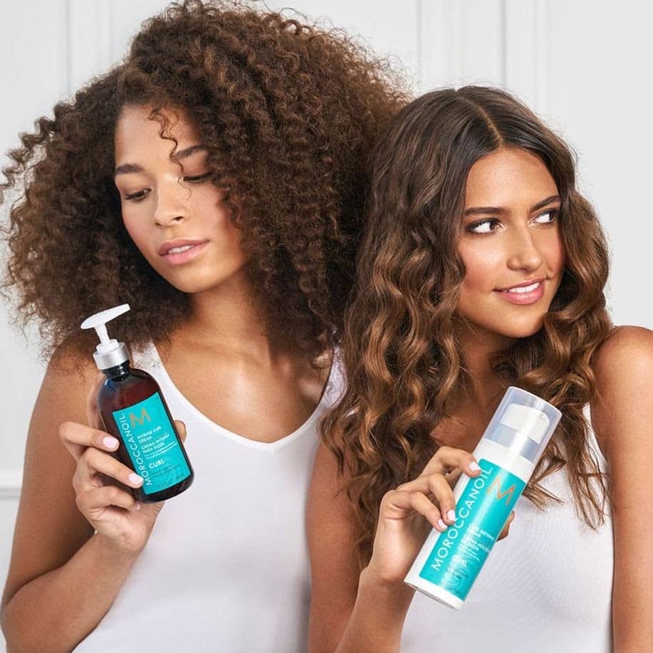 Two beautiful girls with different hair types are holding products from Moroccanoil.