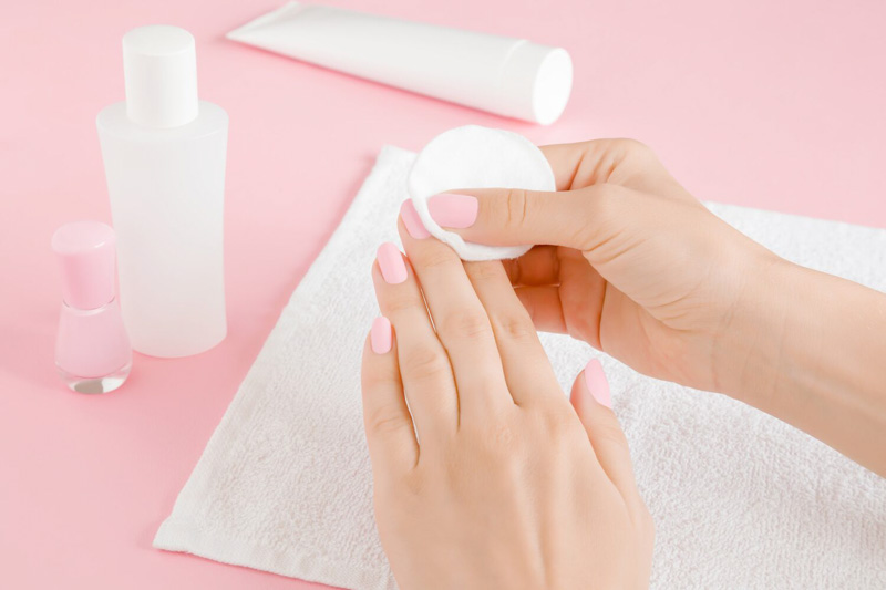 A faceless woman holding nail cotton while while removing dip powder nails in the light pink shade