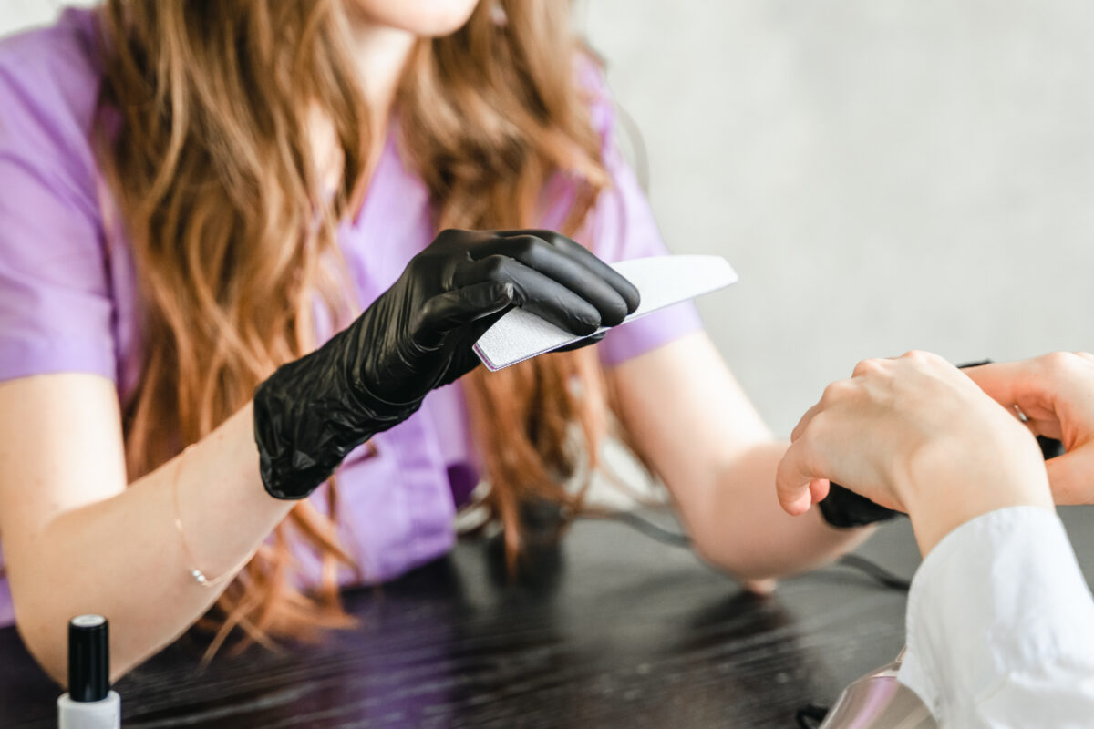 Professional master manicurist at beauty salon. Manicure service, hands treatments, procedures for nails, fingers. Multi-colored nail polish, samples palette, tattoos, cuticle oil, gel uv lamp,gloves.