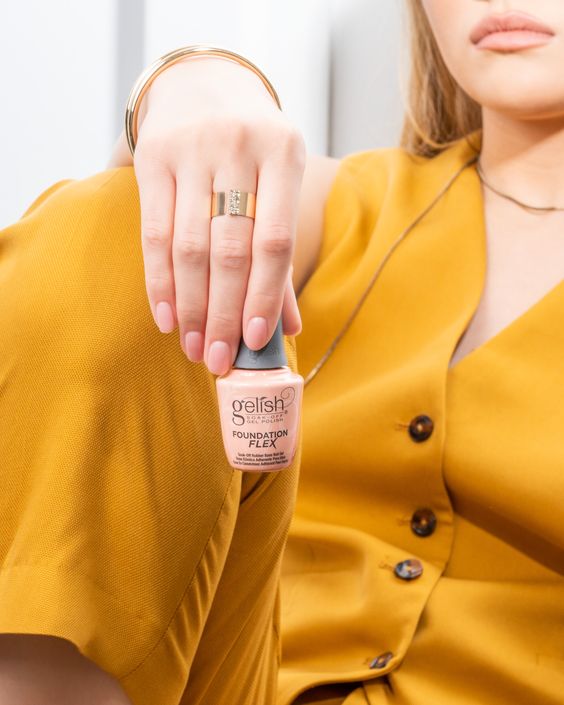 A faceless woman wearing yellow suits and holding a Foundation Flex bottle in the Cover Beige shade
