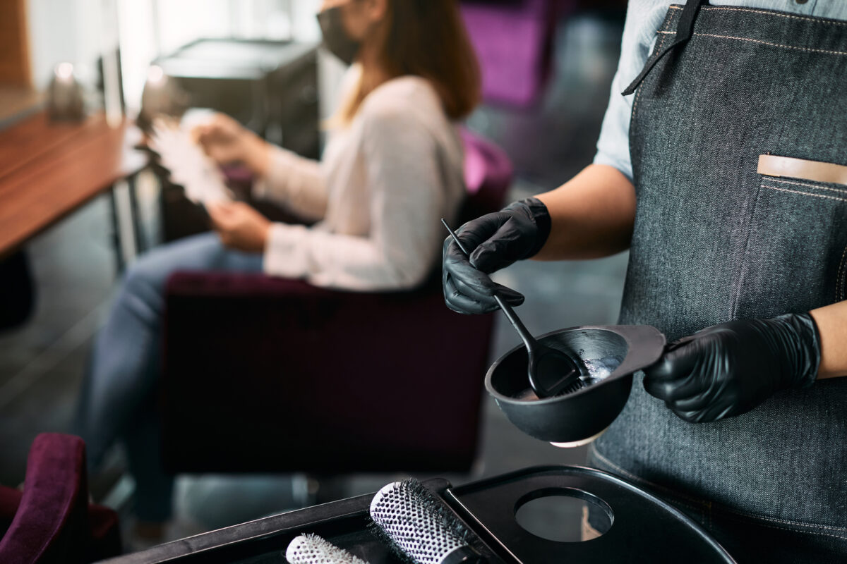 Close-up of hairdresser preparing dye in a container at hair salon.