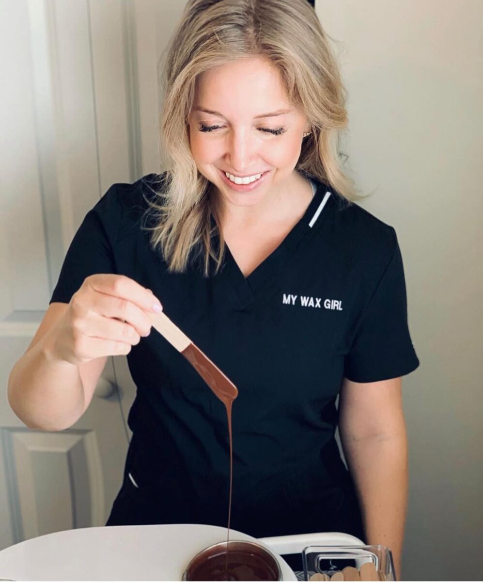 A professional in hair removal services from the Gigi Brand holding a wooden stick with melting wax
