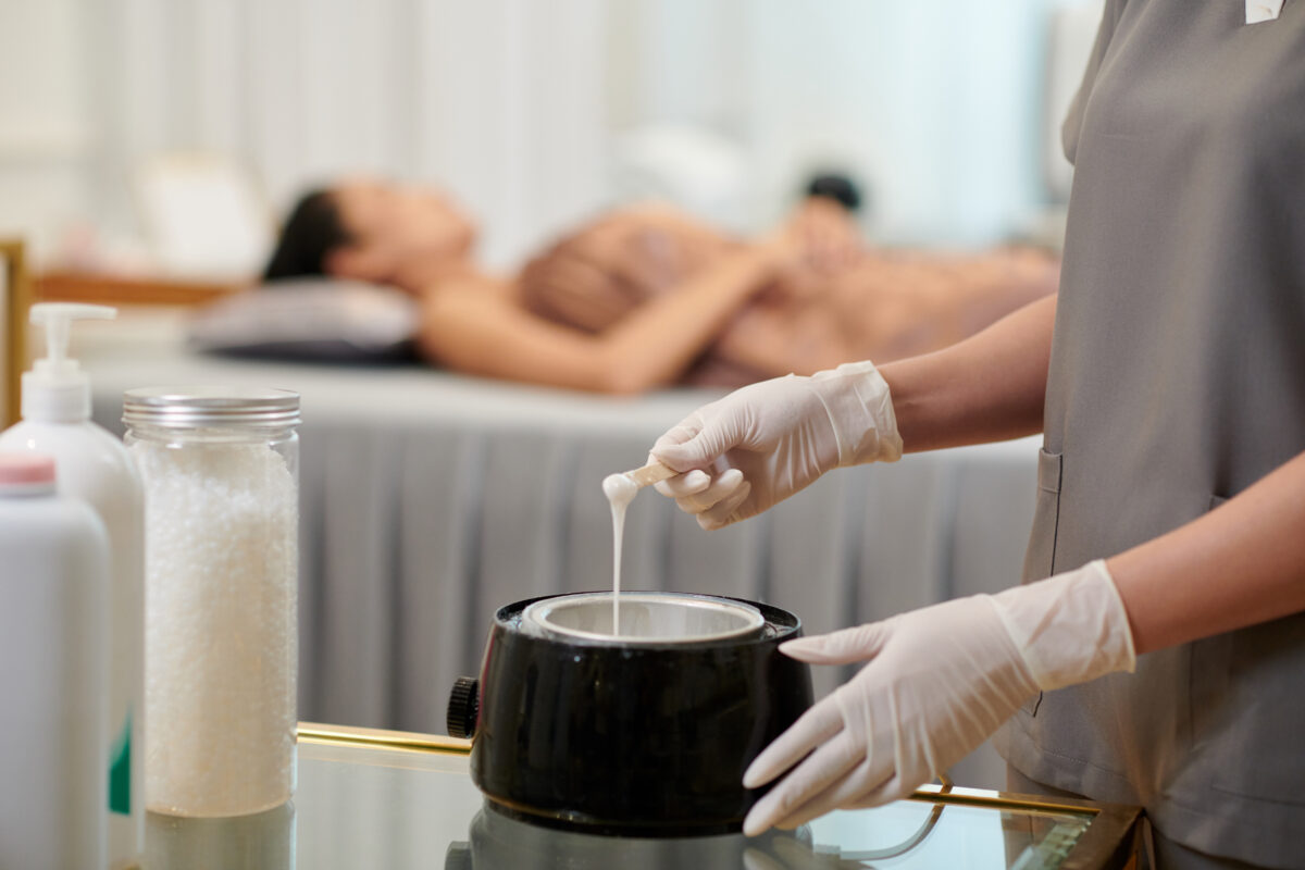 Hands of beautician melting wax for hair removal procedure.