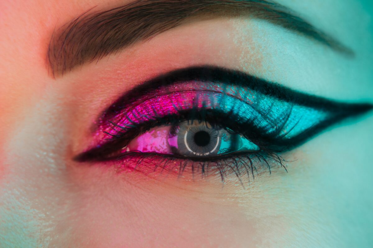 Close up of woman eye with fancy arrow make-up under neon light. Glitter shadows and false lashes. Girl, blue eye