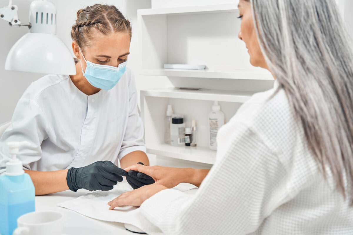 Attentive beautician sitting in front of her client while doing manicure