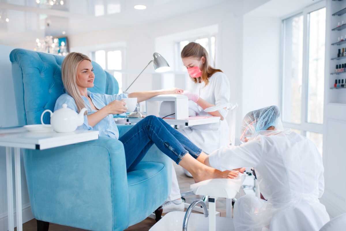 Cosmetology salon, manicure and pedicure procedure. Female client in beauty shop, woman at the cosmetologist, two masters works with fingernails and toenails