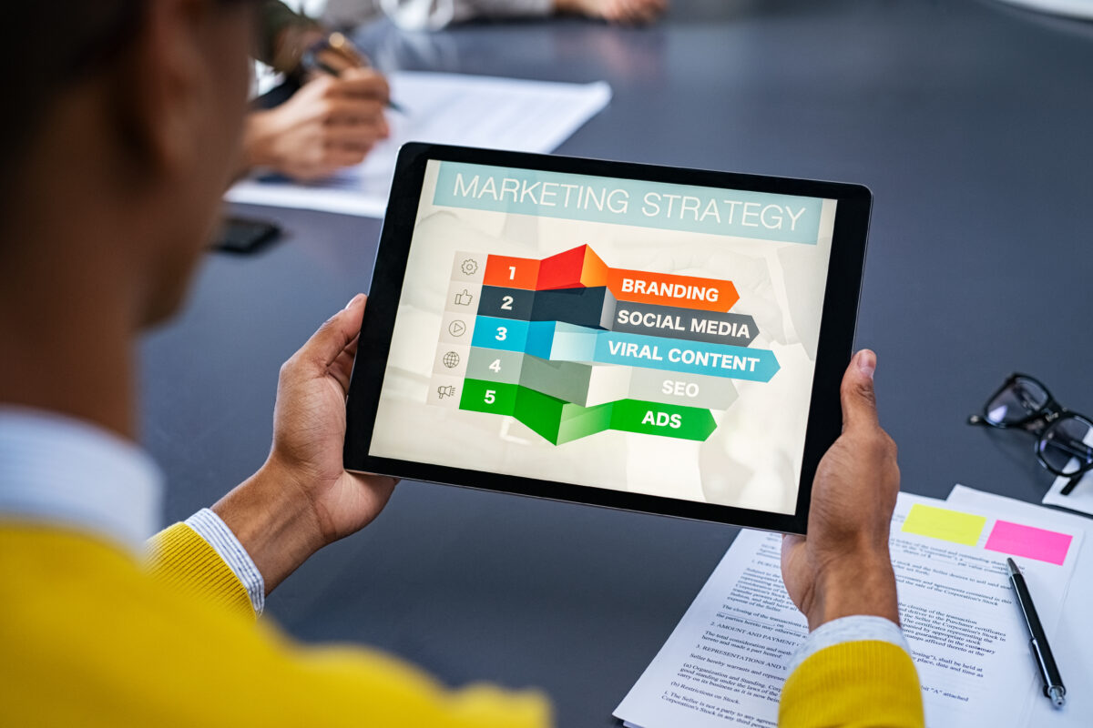 Close-up of a young man using a digital tablet to study marketing strategy for a hair salon. African businessman studying business planning. Rear view of student holding tablet in hands and analyze business material on screen.