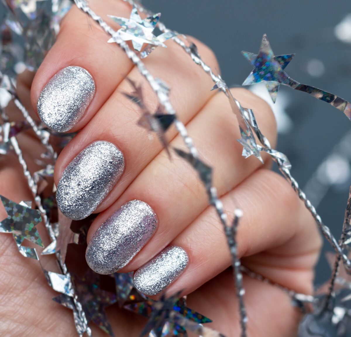 Female hand with beautiful holiday manicure - silver glittered nails with Christmas twisted wire with stars. Selective focus. Closeup view. Blurred background with copy space.