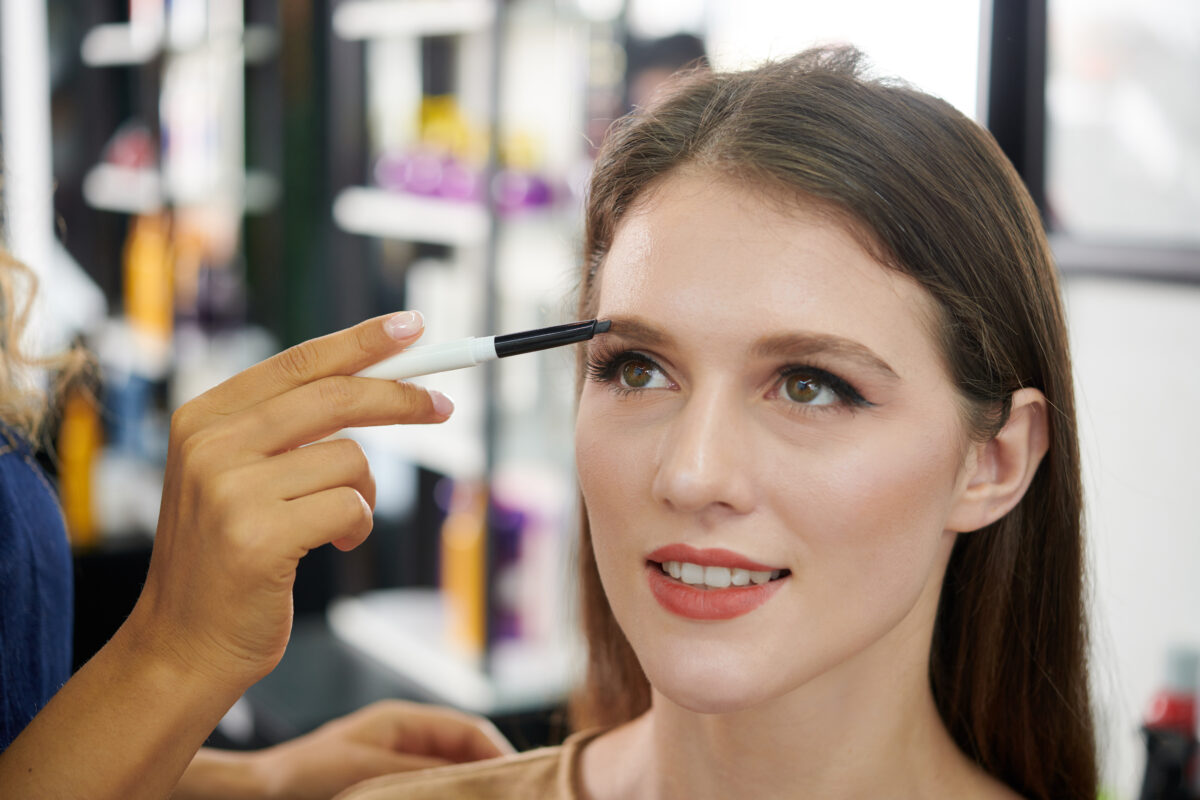 Make-up artist filling brows of young woman with brown pencil