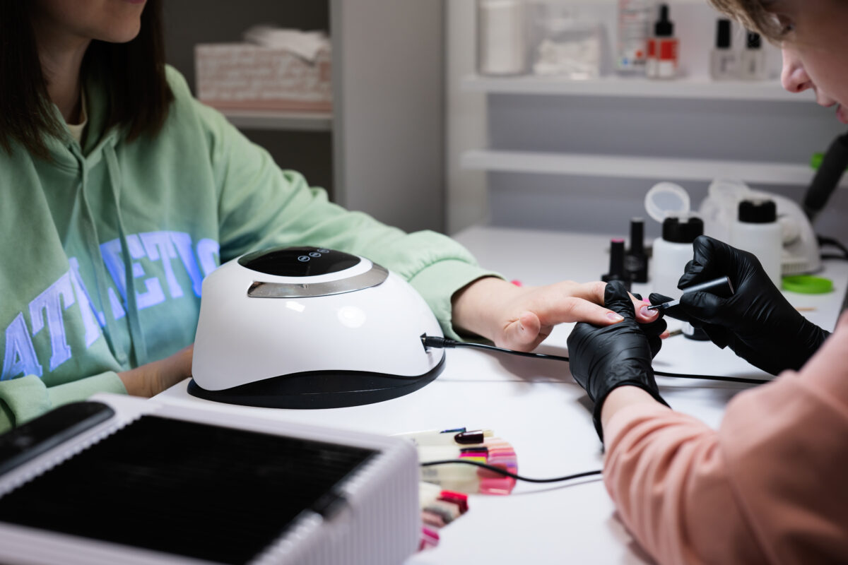 Manicure master working with female client in beauty salon. Drying nails in an ultraviolet lamp.