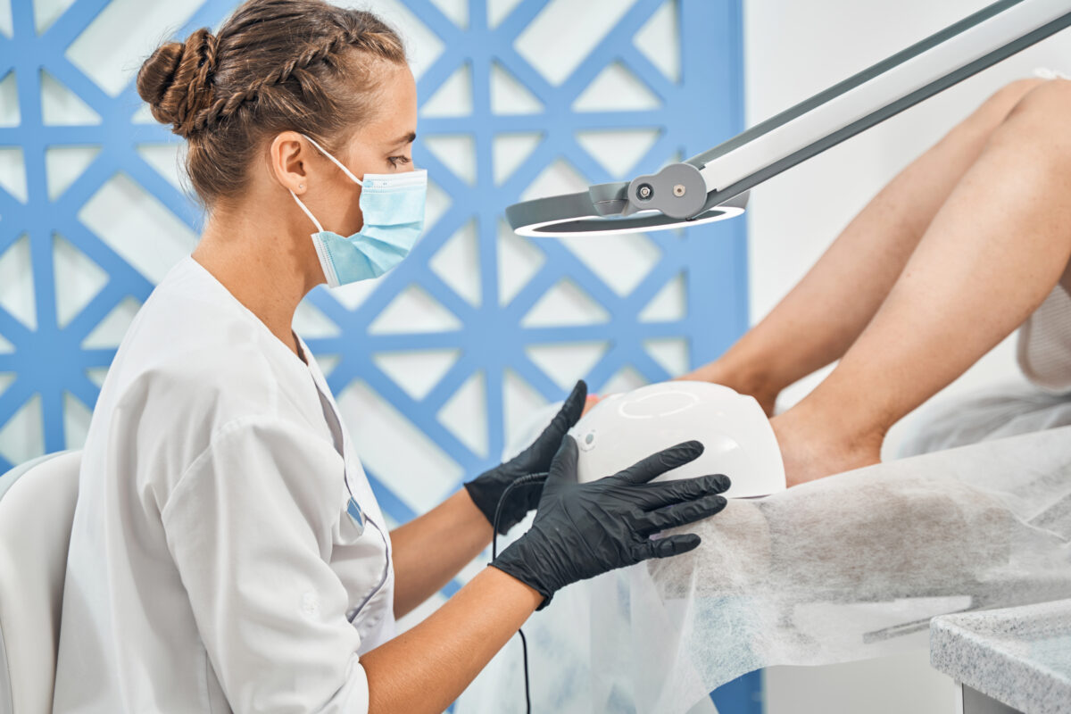 Attentive female person wearing sterile mask on face while working with gel polish