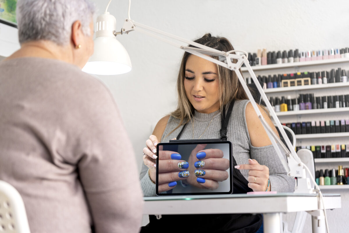 Real female manicurist showing a nail painting design with a tablet in her work place