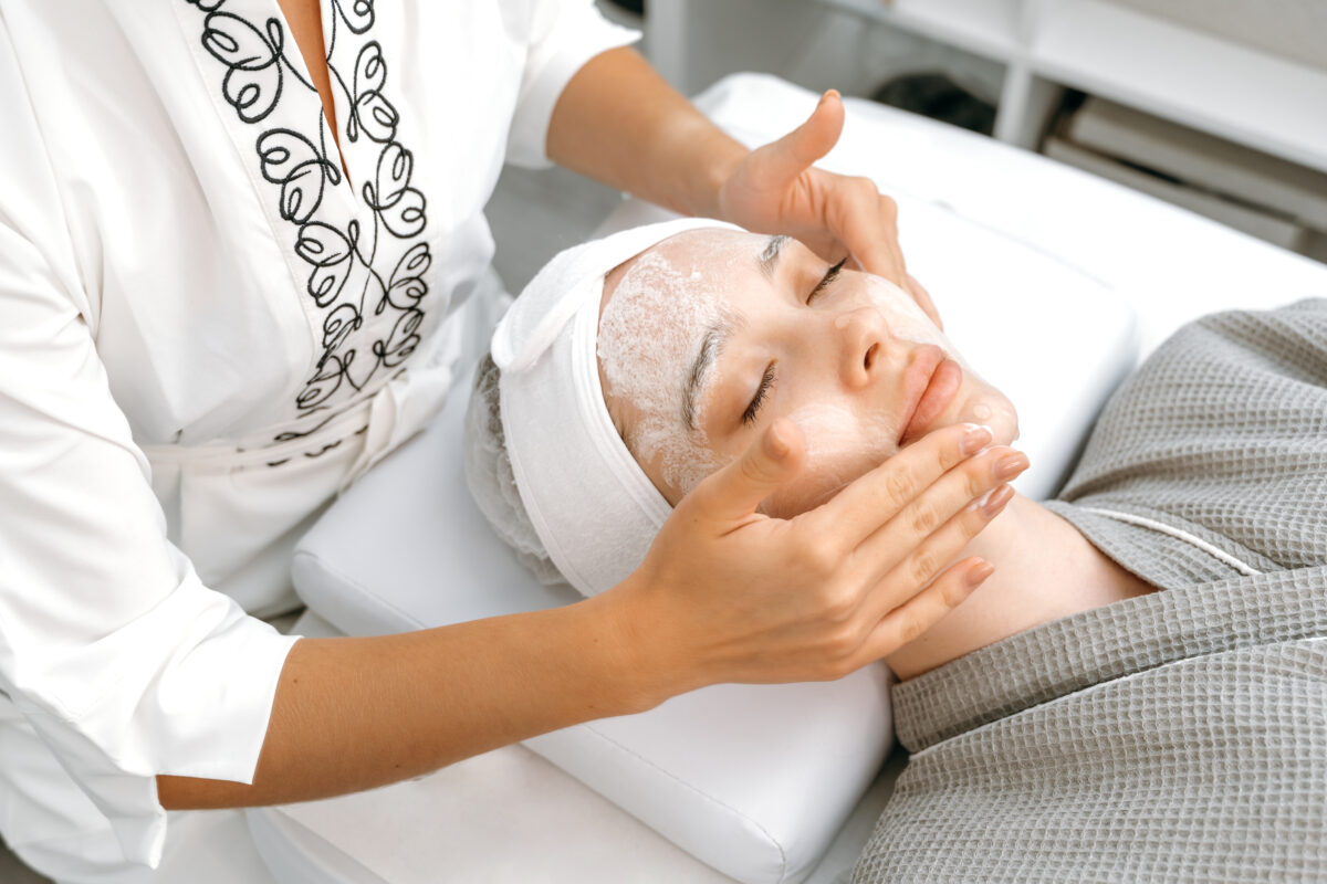 The cosmetologist applies a special cream, scrub, peeling to the face of a pretty caucasian woman to improve the quality of facial skin. Facial skin care procedures in a beauty salon. Beauty treatment
