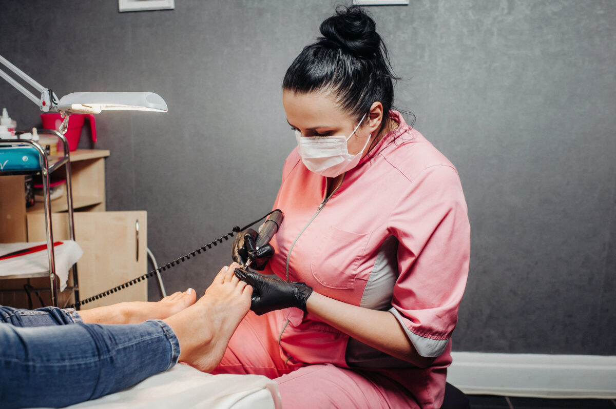 The master makes a pedicure in the beauty salon. The girl in a blue mask and gloves makes cosmetic procedures. Blonde and brunette in a beauty salon. Pure flowers in a tub with water.