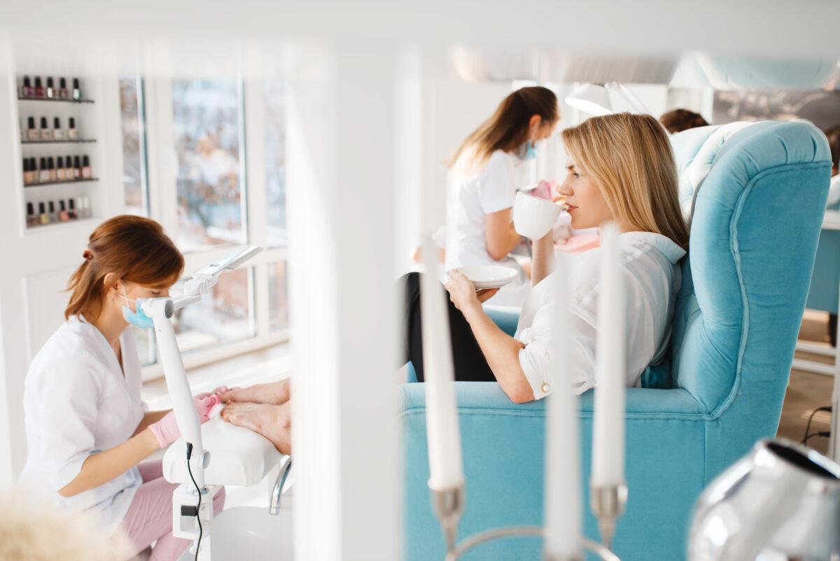 Two women on pedicure procedure in beauty salon. Professional beauticians and female customers, toenail care in spa studio